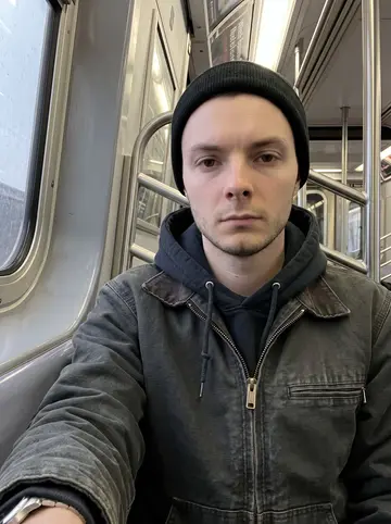 Lucas, AI character: inside a Queens-bound subway car after work, grey window reflection and metal poles behind him
