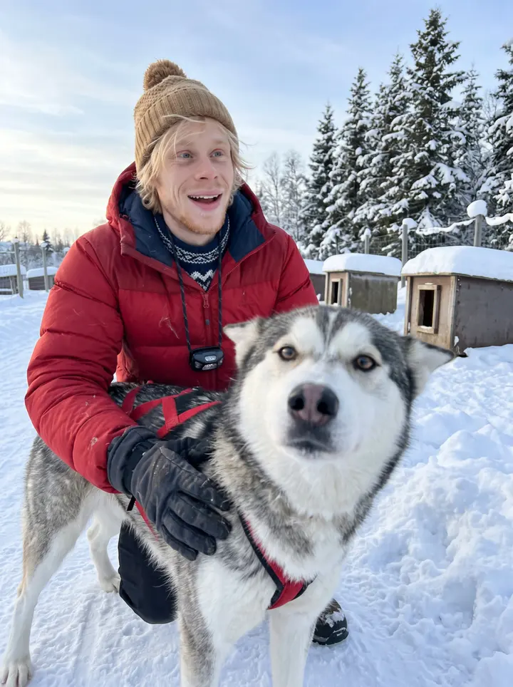 Oskar, AI character: the packed-snow trail behind the kennel outside Tromsø, a row of dog houses and spruce trees blurred behind