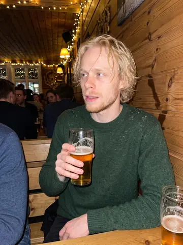 Oskar, AI character: a crowded wooden pub in central Tromsø in December, fairy lights strung along the wall and friends'…