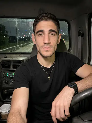 Dmitri, AI character: inside the cab of his tow truck parked on the Stevenson Expressway shoulder at 3am, the Chicago skyline…