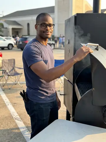 Jamal, AI character: church parking lot in Houston during a brisket fundraiser, standing beside a black smoker