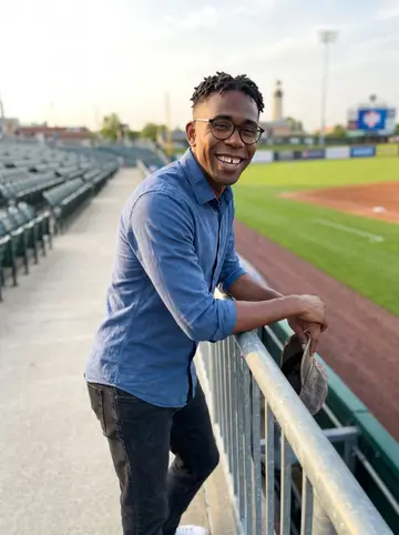Tyrese, AI character: outside the Columbus minor-league baseball stadium after a Saturday game, leaning on a railing with the…