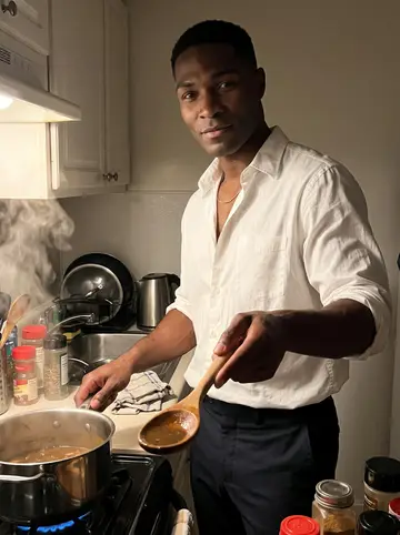 Dominic, AI character: his Brooklyn apartment kitchen at night while he cooks pepper pot soup from his grandmother's Guyanese recipe