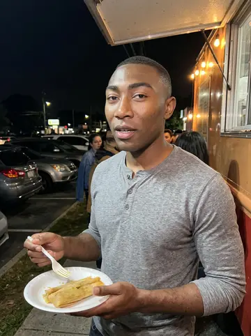 Trevor, AI character: outside a Buford Highway tamales truck after work, small crowd and parked cars behind him