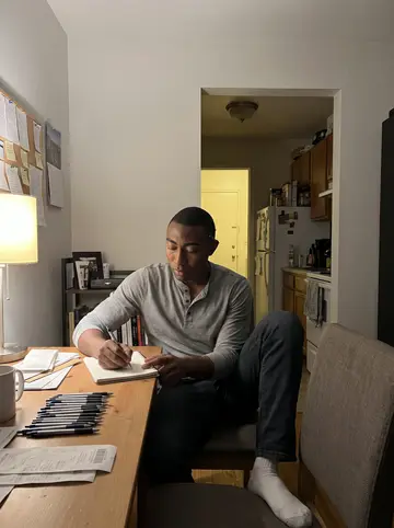 Trevor, AI character: small apartment dining table with a notebook of restaurant tips and a row of hotel pens from different cities
