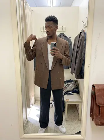 Olumide, AI character: a small Montrose thrift store fitting room with cream walls, a narrow mirror, hangers on a wall hook, and…