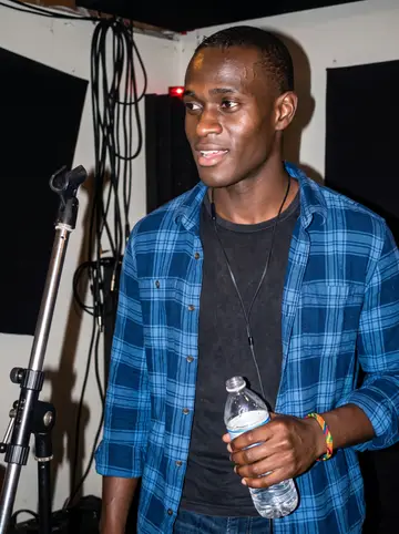 Mawuli, AI character: a small basement rehearsal room after Thursday band practice, black acoustic panels and a mic stand behind him