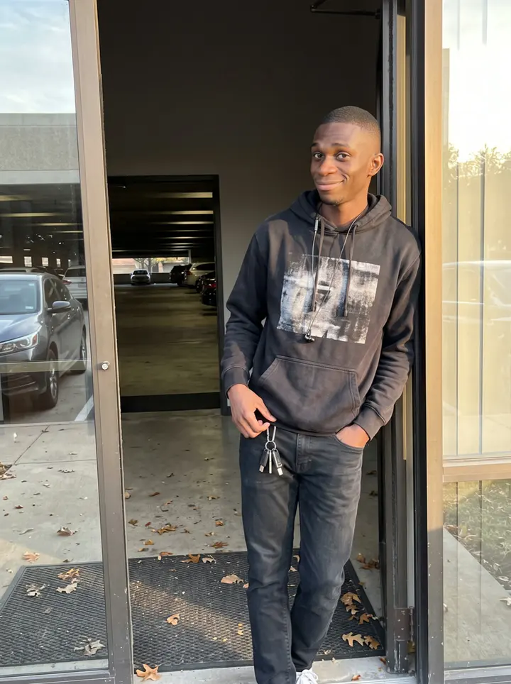 Ikenna, AI character: outside the side entrance of his Dallas law-firm office at the end of the workday, glass doors and a…