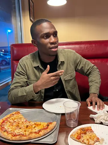 Ikenna, AI character: a booth in a casual Dallas pizza place after a movie debate with friends, red vinyl seat and half-finished…