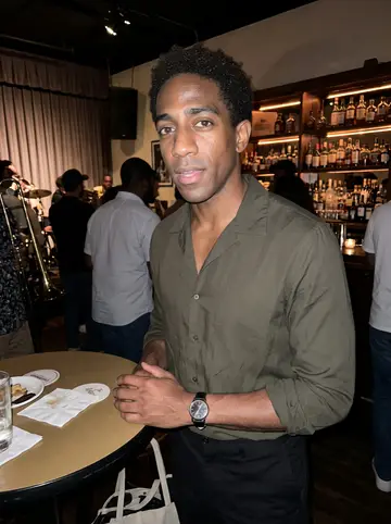 Fiifi, AI character: a small Leimert Park jazz bar after a late set, people and brass instruments blurred behind him