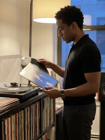 Fiifi, AI character: inside his apartment beside a shelf of highlife and jazz records, turntable glowing beside a floor lamp