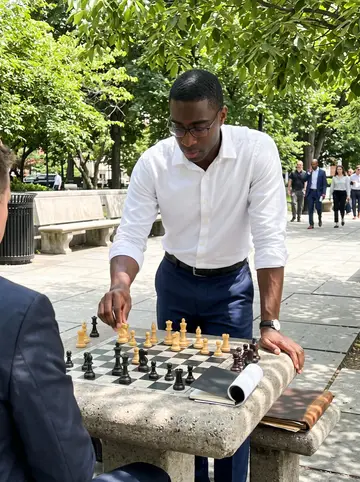 Raheem, AI character: a public chess table in Dupont Circle at lunch, stone benches, trees and office workers in the background