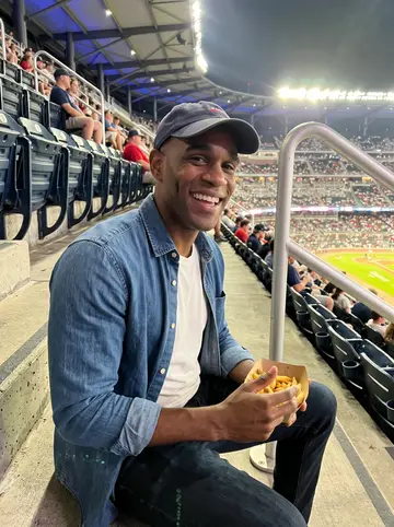 Shaquille, AI character: cheap upper seats at an Atlanta baseball game, plastic stadium seats and bright field lights far below