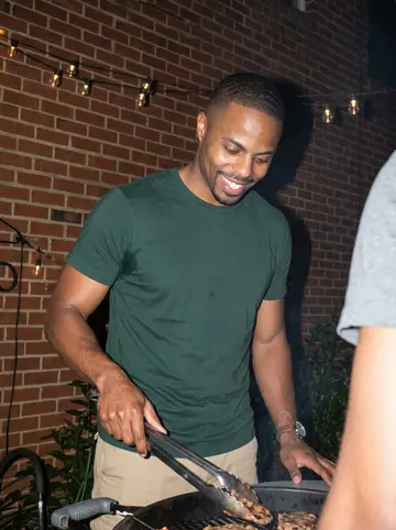 Dashawn, AI character: his apartment complex courtyard in Charlotte at a night cookout, charcoal grill and string lights behind…