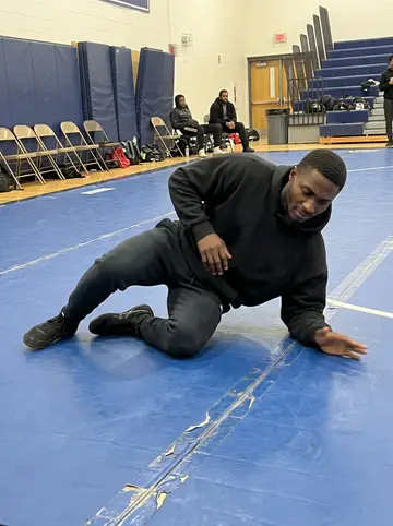 Reginald, AI character: Tuesday night wrestling practice on a blue gym mat in a high school gym in Atlanta