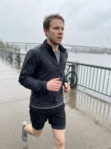 Sander, AI character: the Eastbank Esplanade in Portland during a light spring rain, river and bridges visible behind him