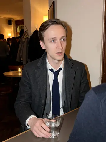 Sandro, AI character: a small Basel jazz bar on a winter night, crowded table near the wall after a friend talked him into…