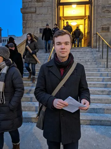 Loris, AI character: outside Milwaukee city hall after a preservation hearing, stone steps and bundled-up neighbors around him