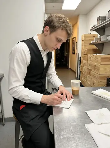 Raphael, AI character: staff corner behind the tasting-menu restaurant in Denver, after service, stainless prep table and stacked…