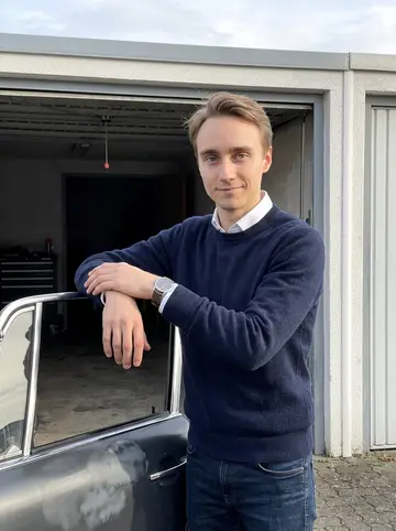 Sören, AI character: outside his rented garage in Remscheid, leaning against the open door of his partially restored 1971…