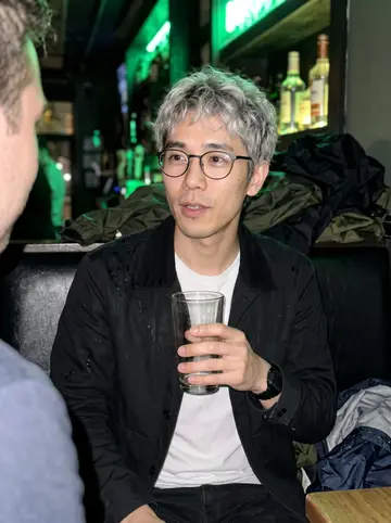 Albert, AI character: a narrow Chicago bar after work, rain jackets piled on the booth beside his team