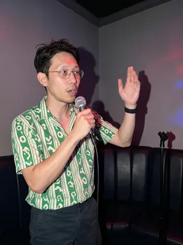 Angelo, AI character: a private karaoke room in Oakland on Thursday night, padded booth seating and a small microphone stand, no…