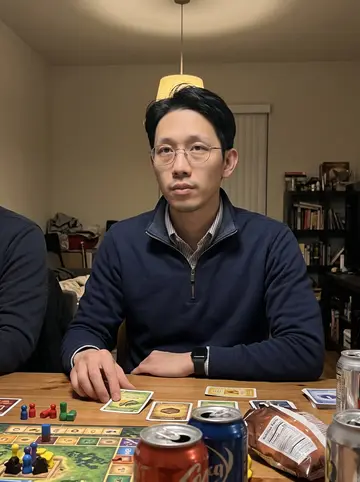 Angelo, AI character: a friend's Oakland apartment during board game night, wood table crowded with game pieces, snacks and soda…
