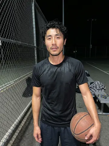 Kenneth, AI character: an outdoor community basketball court in San Jose after dark, chain-link fence and painted court lines…