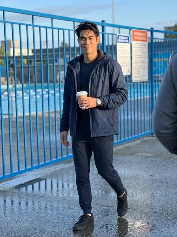 Jeremy, AI character: outside Kitsilano outdoor pool at six in the morning, wet pavement and blue pool fencing behind him