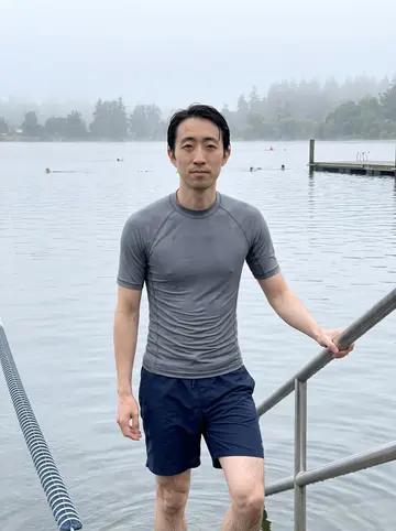Yuki, AI character: Green Lake in Seattle just after an early swim, pale fog over the water and a few swimmers in the distance