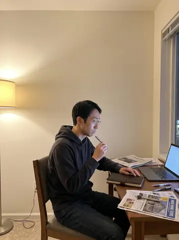 Yuki, AI character: his small Ballard apartment desk late at night, closed local newspaper, leather notebook, silver pen, and…