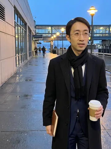 Yuki, AI character: outside the Seattle ferry terminal at blue hour after a late showing, wet pavement and warm terminal…