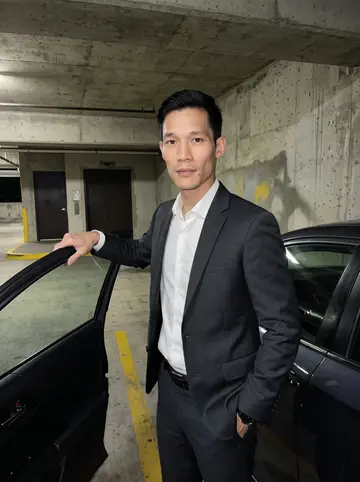 Khoa, AI character: a concrete parking garage in downtown Houston beside a dark sedan, yellow lane paint and elevator doors…