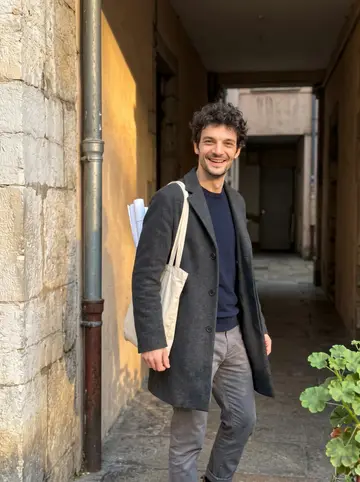 Etienne, AI character: stone spiral staircase inside an old Croix-Rousse silk-weavers' building under renovation: worn steps,…