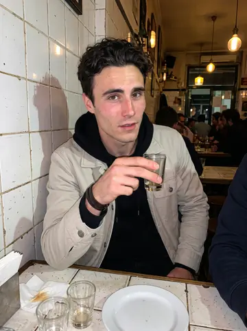 Tristan, AI character: a tiny tiled bar near Santa Apolonia after his late shift, crowded table with small glasses and plates