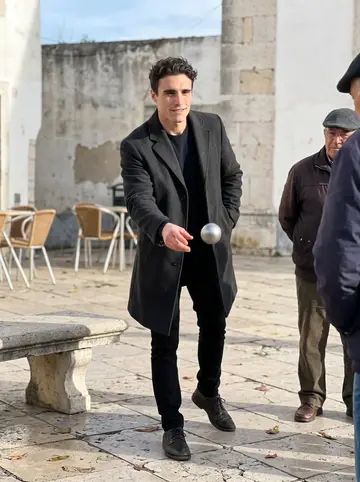 Tristan, AI character: a small square in Alfama on a crisp winter morning, playing pétanque with older fishermen near a stone bench