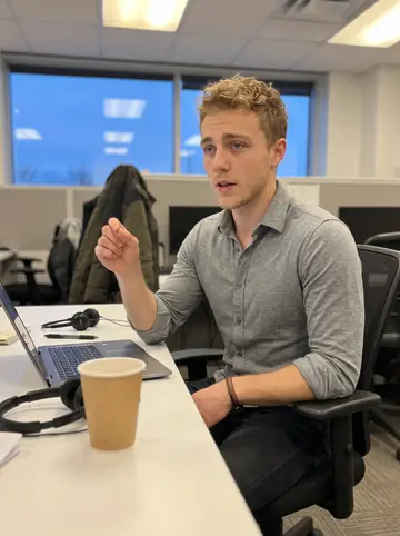 Aymeric, AI character: the break table at a small Montreal sales office, with a laptop, headset and paper coffee cup nearby