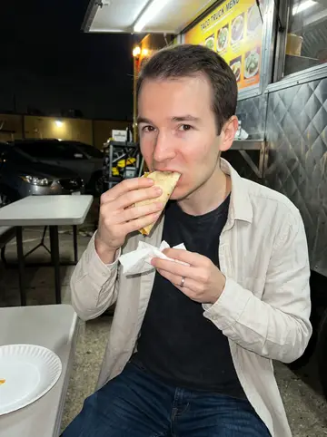 Mathieu, AI character: outside a Houston taco truck on a humid summer Thursday night, plastic tables and parked cars behind him