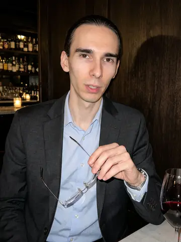 Benoît, AI character: a narrow Chicago wine bar after a client dinner, dark wood wall and small table behind him