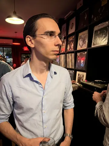 Benoît, AI character: a small record bar in Logan Square during a French chanson vinyl night, shelves of records behind him
