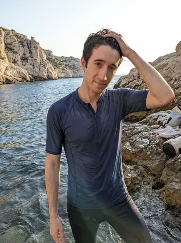 Titouan, AI character: the shallow edge of the Calanques outside Marseille at dawn after free-diving with Yanis, pale limestone…
