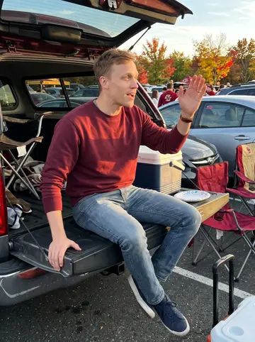 Darren, AI character: a Boston College football tailgate in a parking lot, folding chairs and a cooler behind him