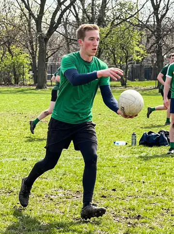 Colm, AI character: a Chicago park field on Saturday morning with other Irish expats playing Gaelic football in the background