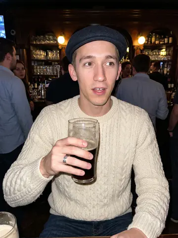 Colm, AI character: a crowded Irish pub in Chicago, dark wood bar behind him and a half-finished pint on the table