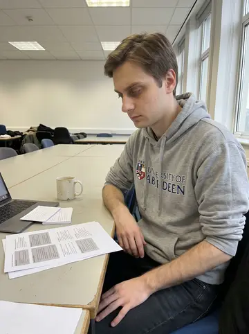 Alistair, AI character: University of Aberdeen medical school study room, anatomy notes, laptop, mugs, and a stack of flashcards…