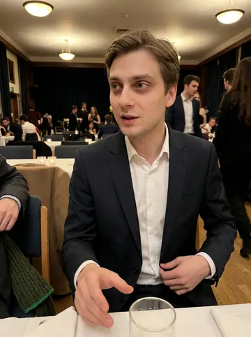 Alistair, AI character: student union hall during the freshers' ball, warm lights, coats over chairs, and blurry students behind him