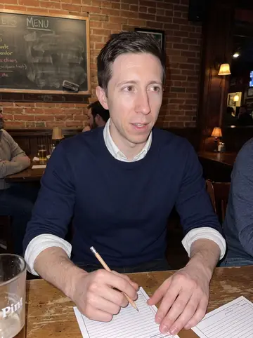 Conall, AI character: Tuesday-night trivia at a narrow Pittsburgh neighborhood bar, score sheets, pint glasses, and a chalkboard…