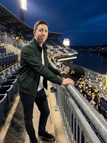 Conall, AI character: upper deck railing at PNC Park after a Pittsburgh Pirates loss, dark river and stadium lights behind him