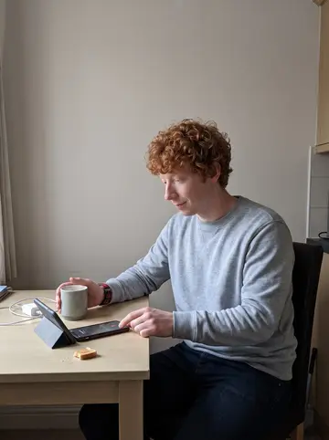 Douglas, AI character: his small kitchen table on a quiet morning, phone propped near a mug while his gran is on speaker