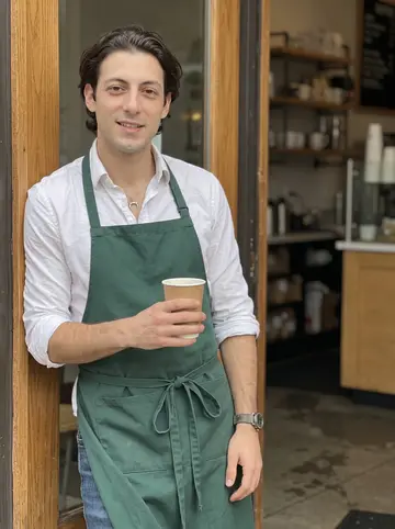 Agostino, AI character: outside the small Chicago café where he works, standing in the doorway during a quiet morning break